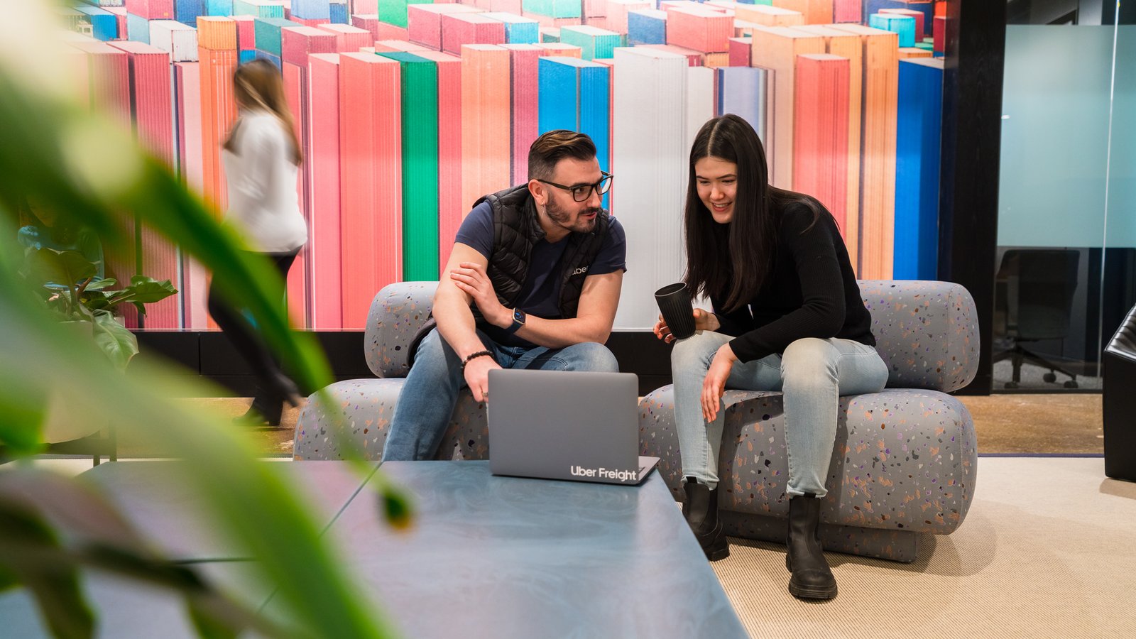 a person and person sitting on couches looking at a laptop