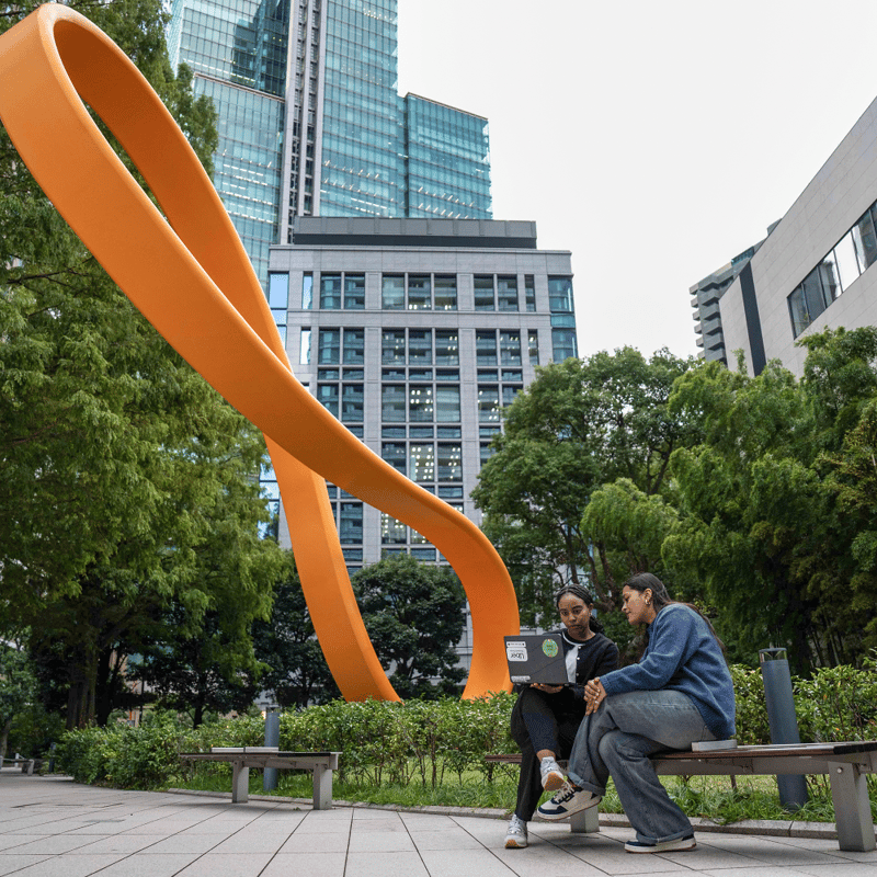 two people sitting on a bench in front of a sculpture