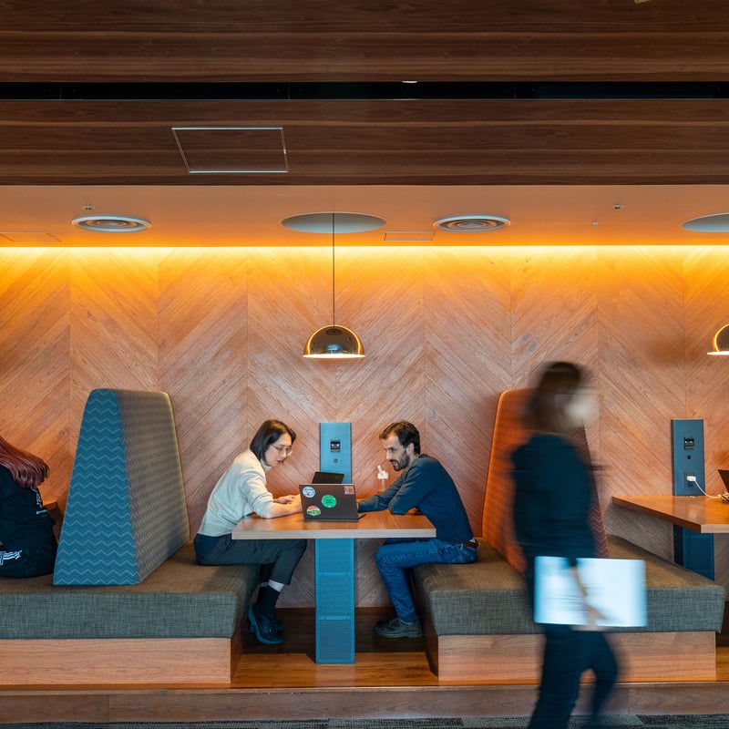people sitting at a table in a room with a wood paneled wall and a couple of people walking